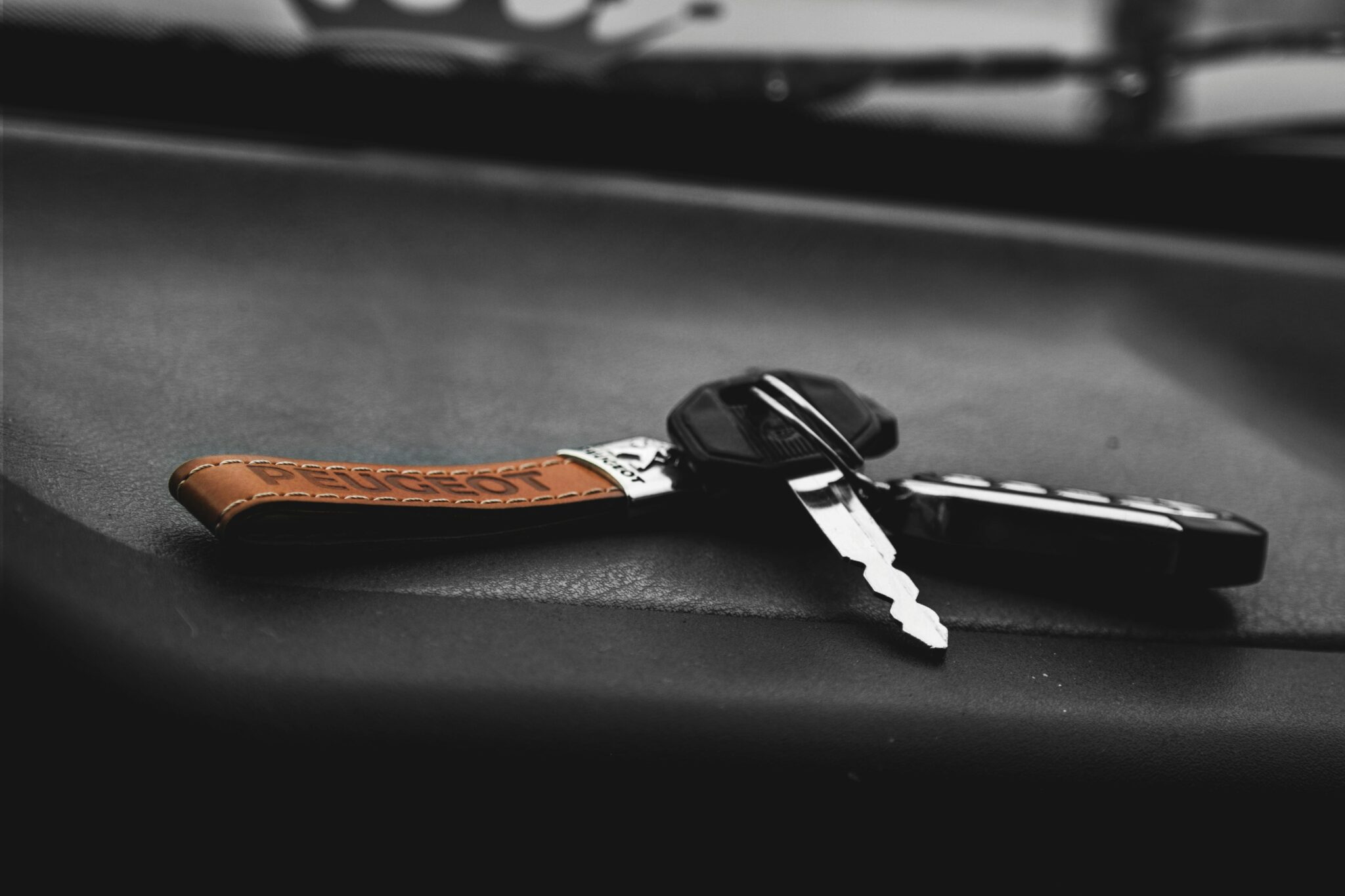High contrast, artistic shot of a car key on a black surface with a leather keychain.